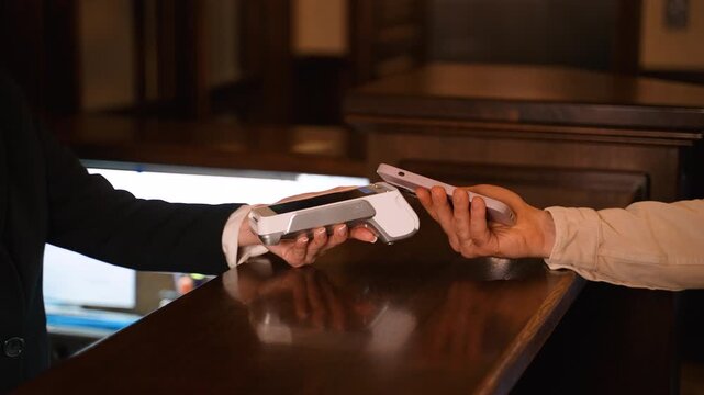 Customer making contactless payment with smartphone at hotel reception desk