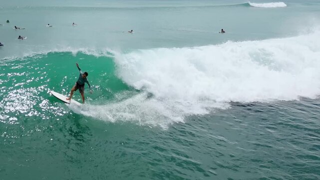 Aerial Surfer Riding Emerald Wave, Carving Powerful Turn Along Reef Break With Cascading Whitewater And Spray,