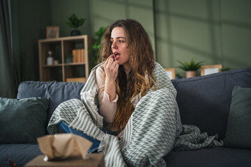 Obraz premium Young woman taking medicine on sofa feeling unwell