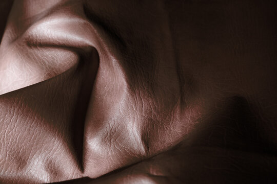 Primer plano de cuero p&uacute;rpura con grano visible, pliegues naturales e iluminaci&oacute;n suave que resalta brillo y textura.sensualidad y resiliencia, simbolizando riqueza t&aacute;ctil, elegancia.