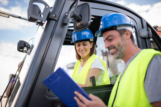 Thirty Five Year Old Woman Driving a Forklift in a Construction Materials Company Wearing Helmet and Reflective Vest