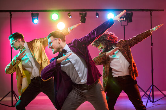 Dancers men group disco party dance celebration fun. Retro performers strike synchronized moves under colorful stage lights, in velvet jackets, bow ties. Joyful celebration concept for brands.
