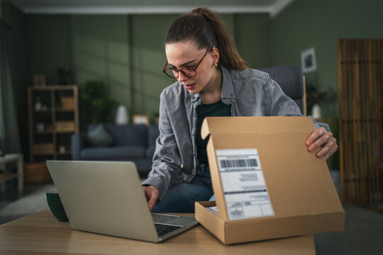 Woman unpacking delivery with laptop showing disappointment