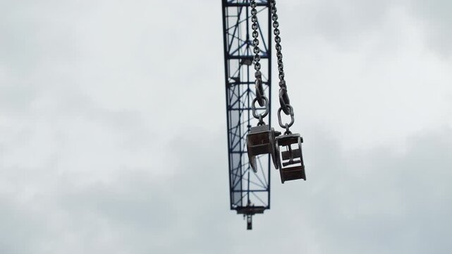 Crane lifting clamps hanging on chain against cloudy sky