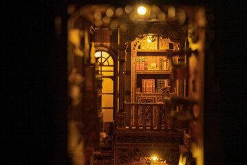 Magical wooden book nook miniature library diorama glowing with warm lights in the dark. Intricate bookshelf alleyway with tiny books, ladder, and vintage decor. Enchanting handmade room box model. © Alisa