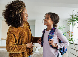 Mother helping daughter to get ready for school, helping her with backpack and books,hugging and...