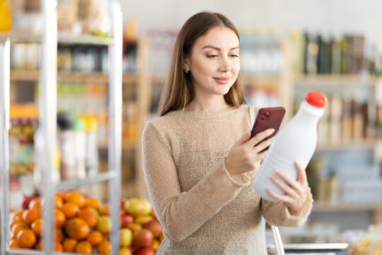 Girl customer at shop scan QR code on milk bottle using phone camera. Client inspect item, manufacturer information of product using application. Visitor examines product by mobile app