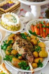 A set and decorated Easter table with festive appetizers, pastries, a baked leg of lamb and painted eggs