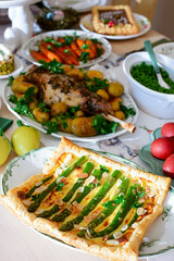 A set and decorated Easter table with festive appetizers, pastries, a baked leg of lamb and painted eggs