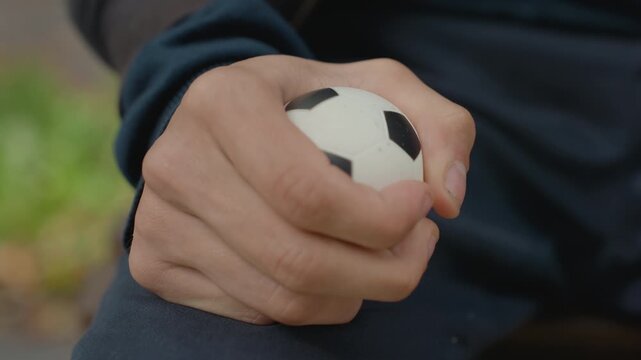 outdoor closeup hand squeezing foam ball on park bench, casual man taking mindful break, green bokeh background, relaxed grip and breathing rhythm, stress relief practice with portable soccerthemed