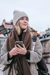 Winter city wanderlust: female tourist walking historic Warsaw old town, pastel facades and holiday lights, cozy coat, scarf and beanie. Urban sightseeing, slow travel, sustainable Europe escape eco.
