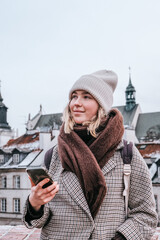 Winter city wanderlust: female tourist walking historic Warsaw old town, pastel facades and holiday lights, cozy coat, scarf and beanie. Urban sightseeing, slow travel, sustainable Europe escape eco.