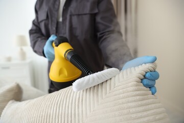 Pest control worker cleaning sofa with steam cleaner indoors, closeup