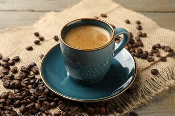 Aromatic coffee in cup and roasted beans on wooden table, closeup