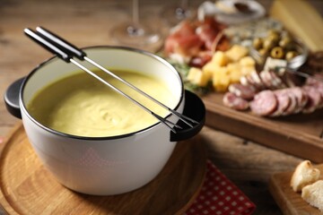 Fondue pot (caquelon) with melted cheese and snacks on table, closeup