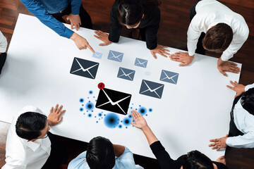 A diverse group of business professionals discusses email communication strategies, engaging collaboratively around a white table with email icon visuals, showcasing teamwork and innovation. Trope