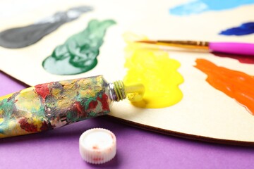 Obraz premium Palette with watercolor paints, tube and brush on purple background, closeup