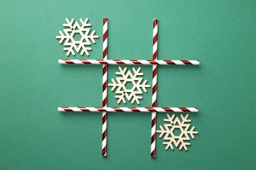 Tic tac toe game made with wooden snowflakes on green background, flat lay