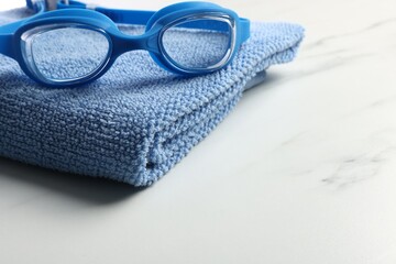 Protective goggles and towel on white marble table, closeup with space for text. Swimming...