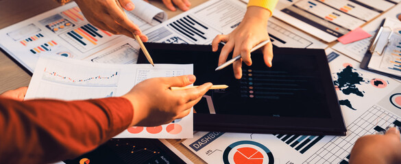 Engaging business meeting scene featuring hands analyzing data on a tablet alongside colorful charts and documents, showcasing collaboration and strategic planning efforts. SACTR