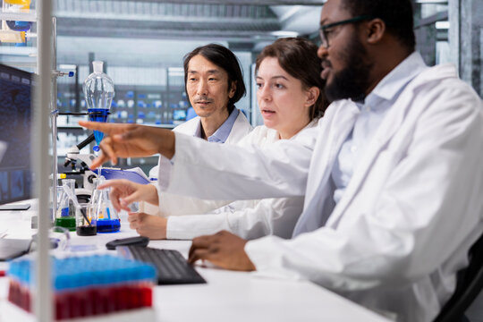 Multiethnic team in laboratory using computer program for DNA data analysis. Diverse research facility coworkers using bioinformatics genomics software on PC in modern lab - Powered by Adobe