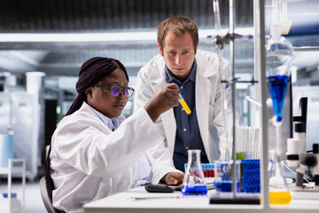 Diverse coworkers in biolab analyzing flasks and vials for chemical experiment. Team using laboratory tools for innovation in biochemistry, biology and genetics research, testing.