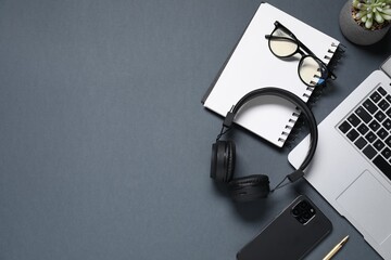 Headphones, smartphone, stationery, glasses, laptop and floral decor on black background, flat lay. Space for text