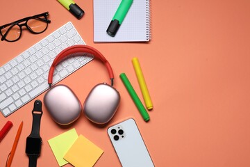Headphones, computer keyboard, smart watch, smartphone, glasses and stationery on coral background,...