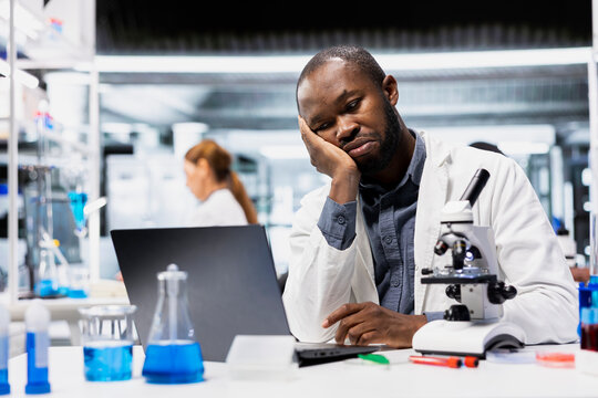 Lab researcher frowning, disappointed by experiment results data. Stressed african american man upset by inconclusive study results and research progress when documenting findings on laptop