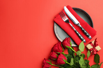 Beautiful table setting with roses and gift on red background, flat lay. Space for text