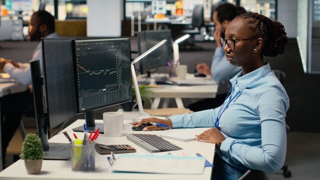 Day trader analyzes stock market price charts, taking notes to make informed buy and sell decisions. Stockbroker writing down analysis insights, placing orders using trading platform