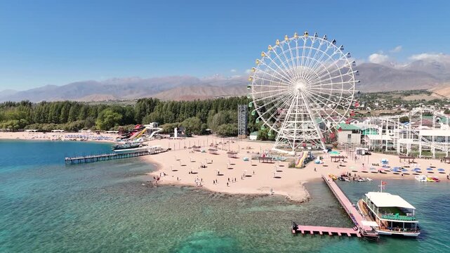 Ferris wheel by Issyk-Kul Lake with scenic mountains in the background, a popular tourist spot.