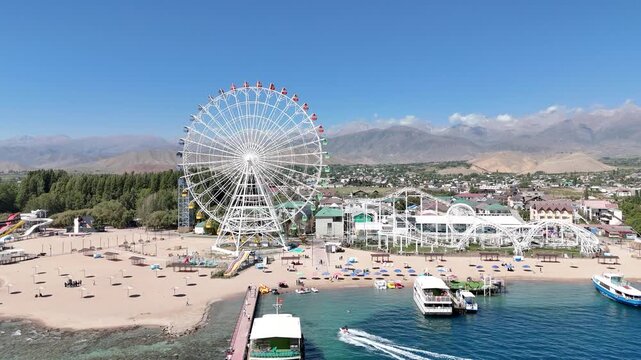 Ferris wheel by Issyk-Kul Lake with scenic mountains in the background, a popular tourist spot.