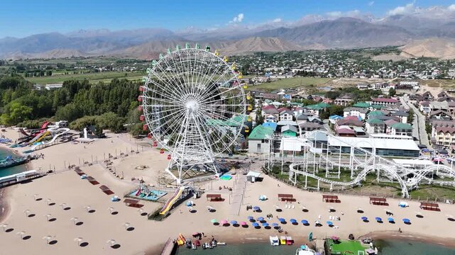 Ferris wheel by Issyk-Kul Lake with scenic mountains in the background, a popular tourist spot.