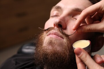 Barber styling man's mustache with wax in barbershop, closeup. Space for text