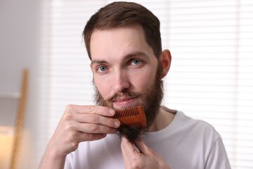 Handsome man combing his beard at home