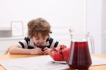 Little boy drinking fresh pomegranate juice at table indoors