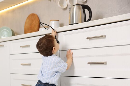 Child safety at home. Little boy reaching for electric kettle in kitchen