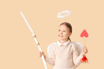 Naklejka premium Cute little girl dressed as cupid with bow and arrow on beige background. Valentine's Day celebration