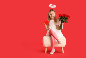 Fototapeta premium Cute little girl dressed as cupid with bouquet of beautiful rose flowers and gift box sitting on pouf against red background. Valentine's Day celebration