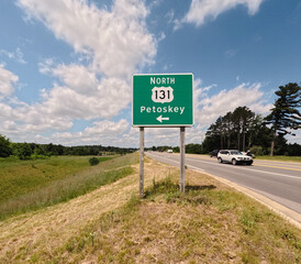 Northbound US-131 Highway Sign Pointing to Petoskey, Michigan. Set against a blue sky with fluffy white clouds, situated on the side of the road exit ramp. A major transportation corridor in Michigan.