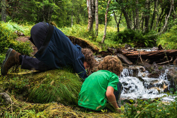 Two boys crouch beside a stream in Innerdalen, playing with water while enjoying nature. The brothers explore their surroundings during a hike in the Innerdalen mountain valley Norway © Dylan