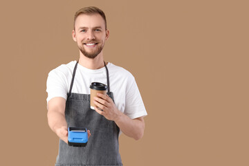 Male barista with coffee cup and payment terminal on beige background