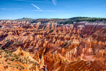 A beautiful canyon with a blue sky above it. The canyon is filled with red rocks and trees, creating a serene and peaceful atmosphere. The blue sky contrasts with the red rocks