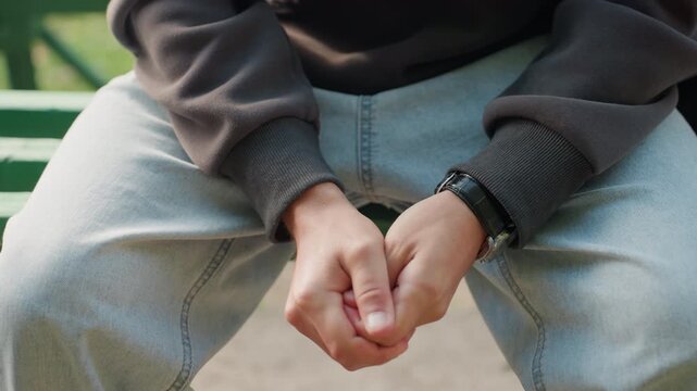 hands on park bench, wearing jeans. closeup of male hands fidgeting with watch and sweater cuff in quiet urban park, afternoon light, contemplative anxious mood, subtle finger tension and idle
