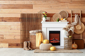Naklejka premium Interior of living room with folding screen, ladder, suitcase, wicker table and autumn decorations on fireplace near wooden wall