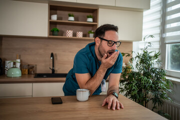 Tired medical professional yawning at kitchen counter with coffee