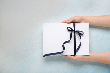 Female hands holding blank card with bow on light blue background