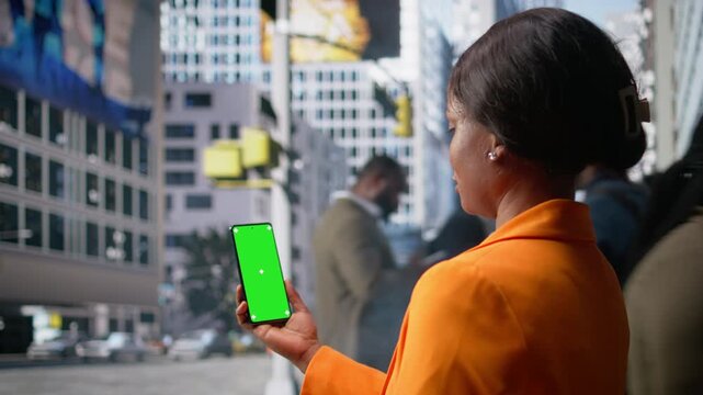 Vertical isolated screen on phone held by black woman near group of pedestrians walking outdoors in the business district. City movement, active lifestyle and the realistic street life. Camera A.