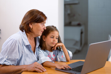 Grandmother and granddaughter using laptop together at home, enjoying time learning and exploring technology, showing family bond and generational connection